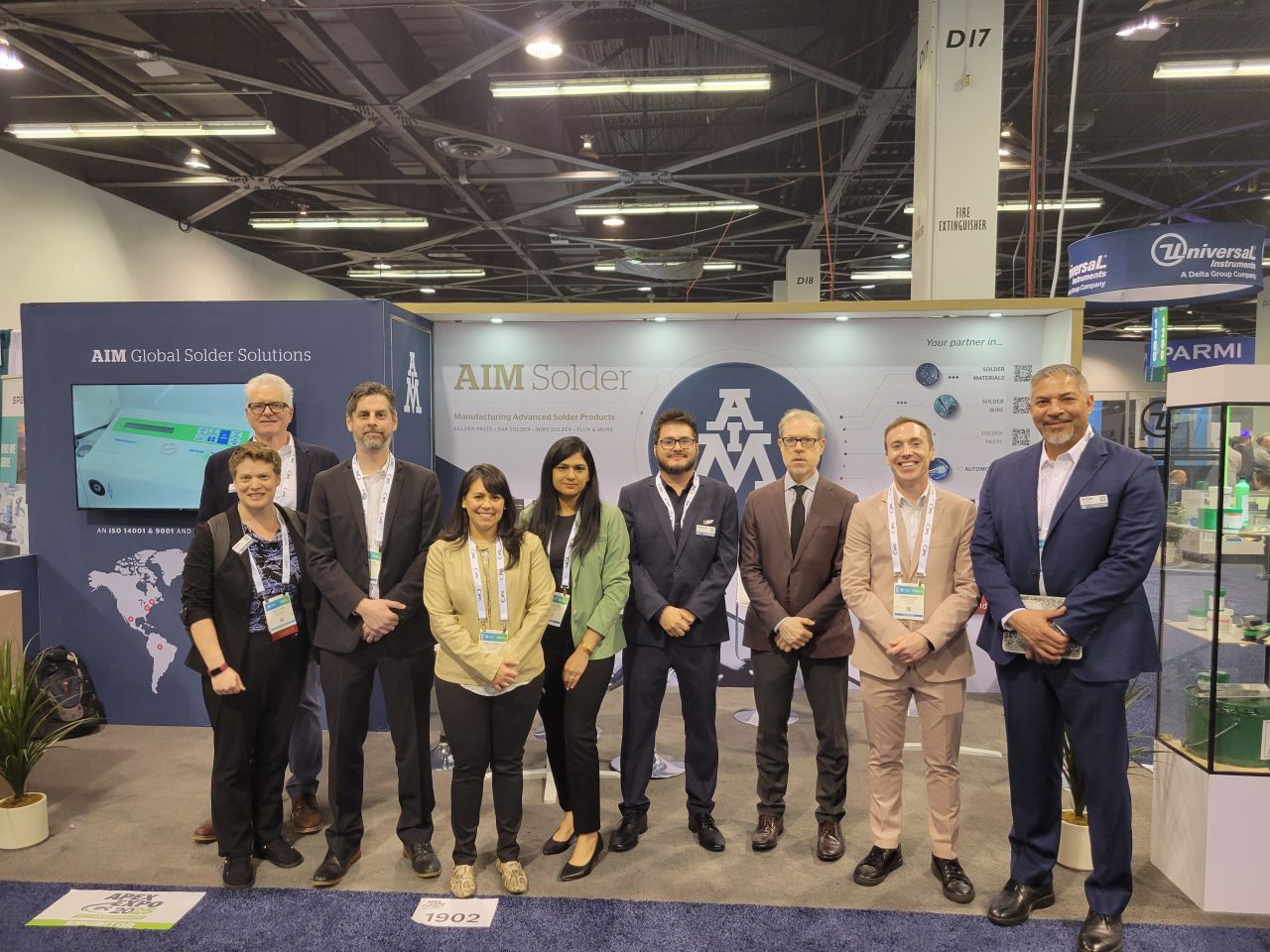 A group of people standing in front of the AIM Solder IPC APEX booth